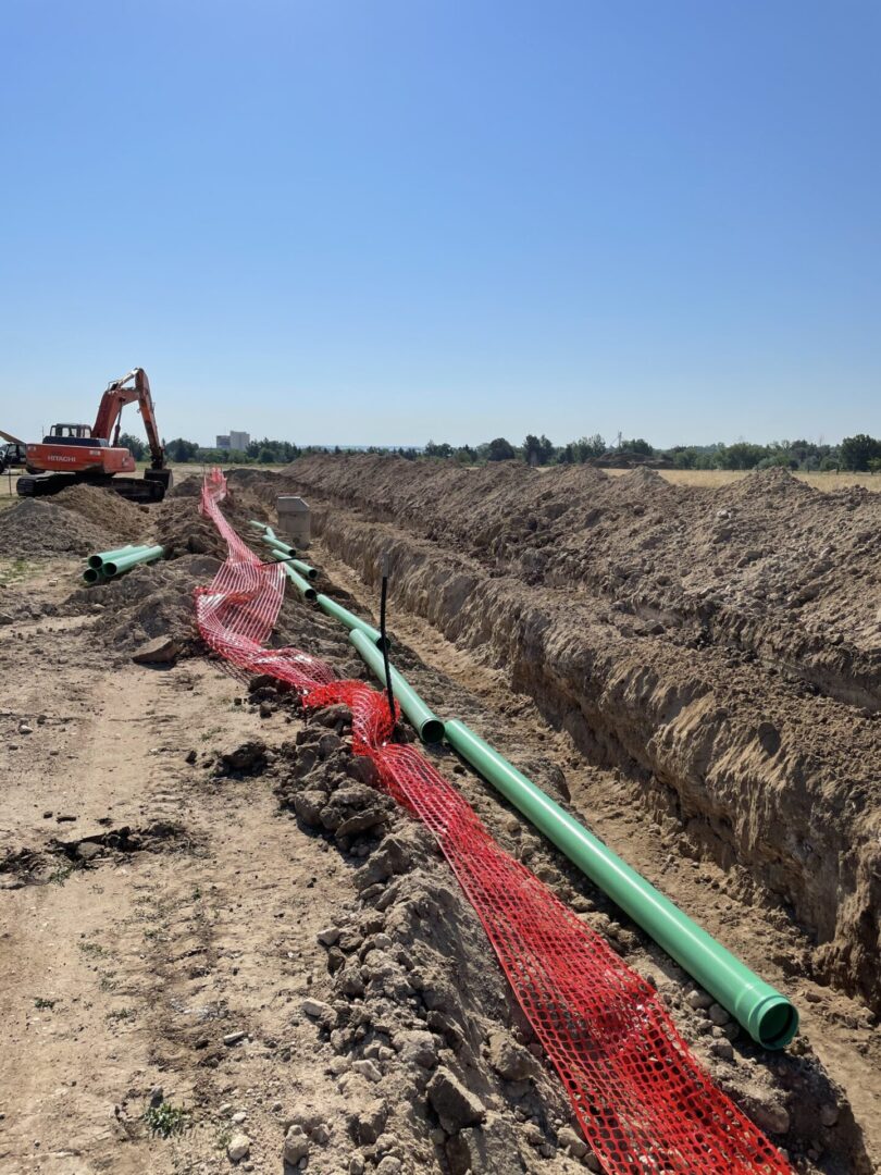Construction trench with green pipes and excavator